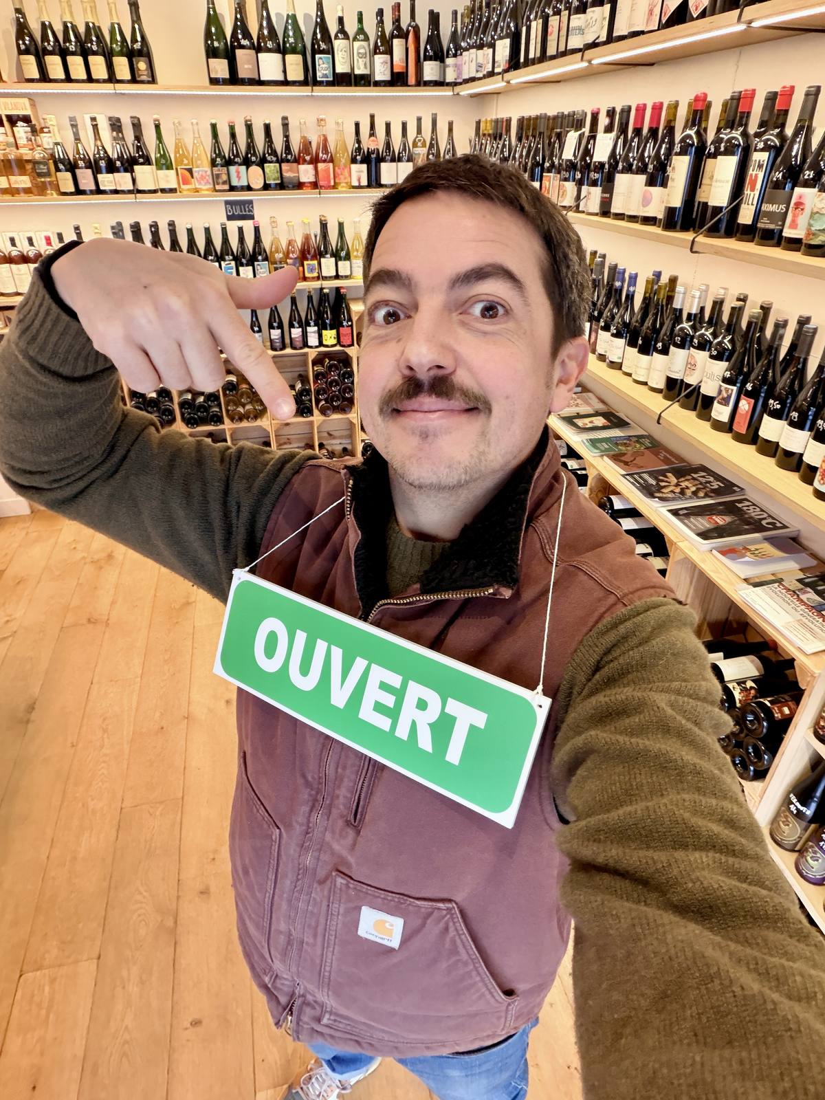 Nicolas Demarty, caviste, avec le panneau Ouvert dans la cave Maison Wino